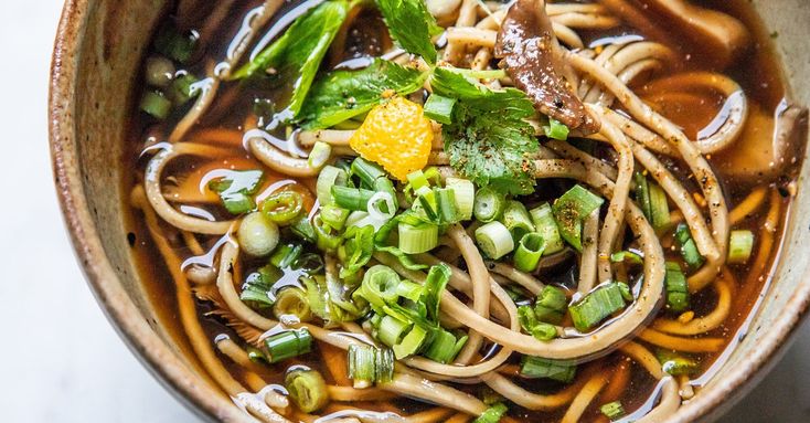 a bowl filled with noodles and vegetables on top of a white countertop next to chopsticks