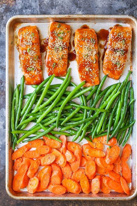 salmon, green beans and carrots are arranged on a baking sheet with seasoning