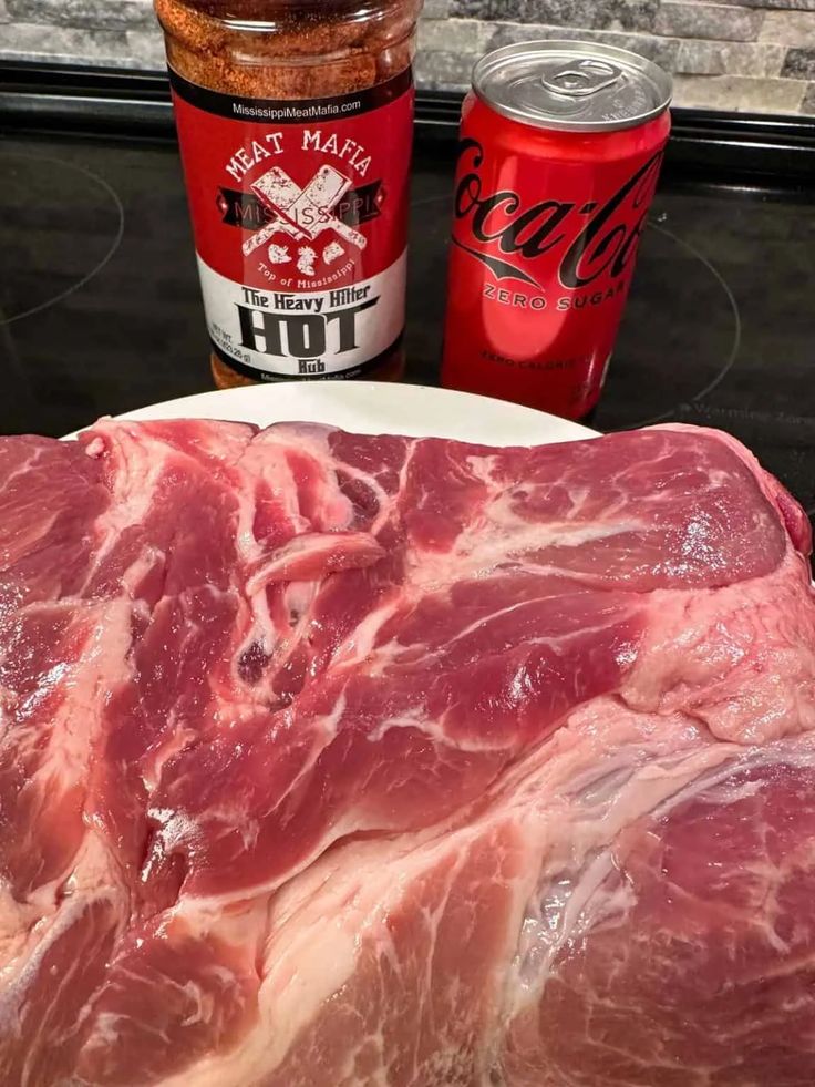 raw meat sitting on top of a white plate next to two cans of sodas