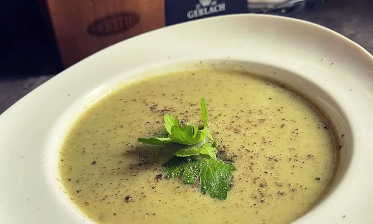 a white bowl filled with soup and garnish on top of a table next to a bottle