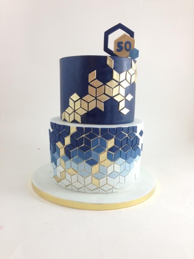 a three tiered cake decorated with blue and gold geometric shapes on a white plate