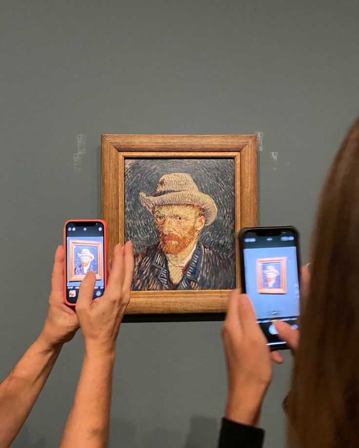 two people holding up their cell phones to take pictures of an art work on the wall