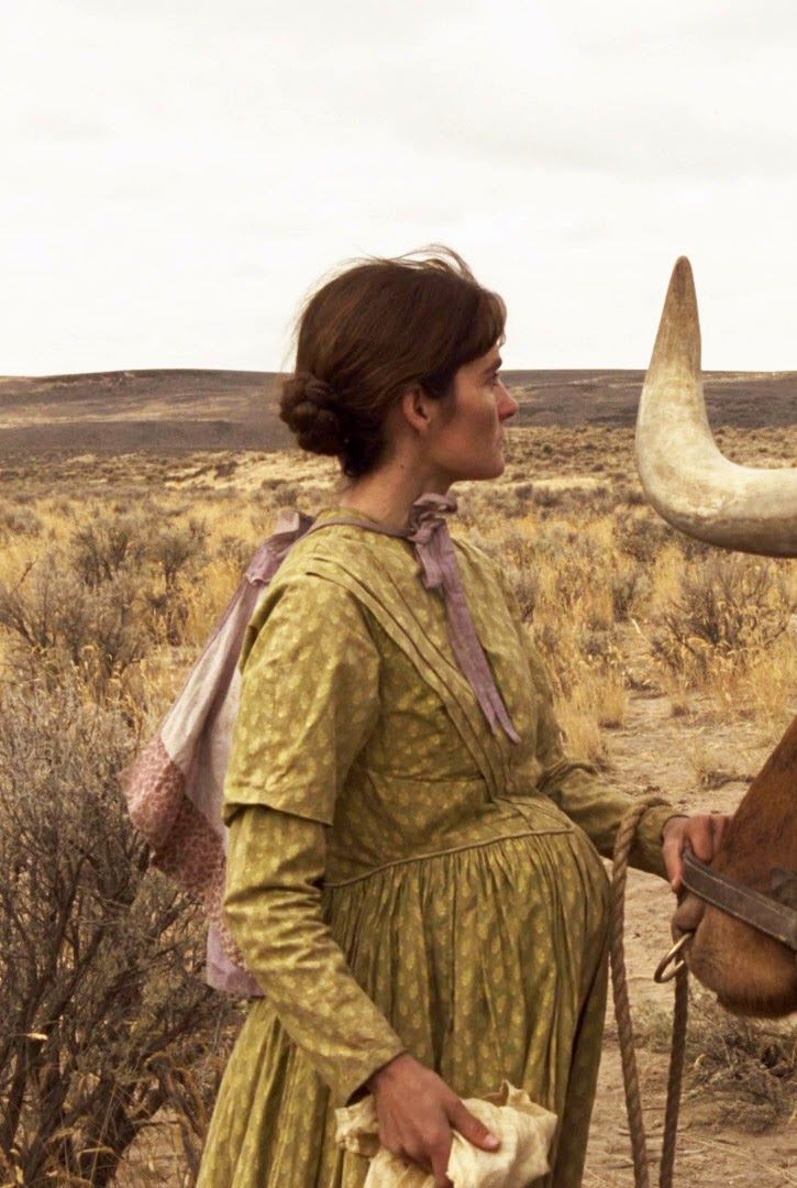 a woman standing next to an animal with long horns on it's head and wearing a green dress