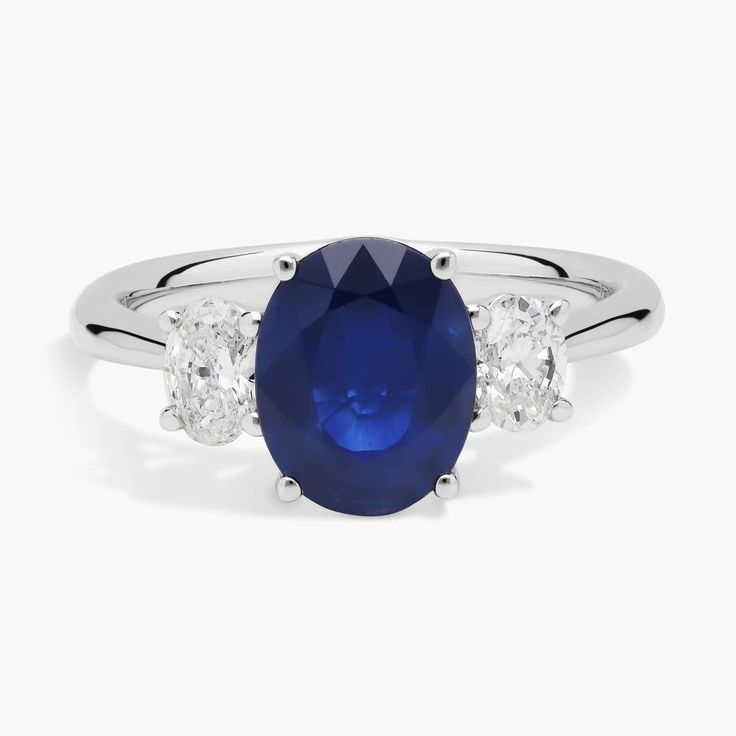 Simple and stunning, this ring features a vividly blue oval-cut sapphire nestled between two stunning oval-cut diamonds. It is crafted from 14k white gold that promises lasting luxury and a bright gleam. Blue Oval Diamond Ring With Polished Finish, Oval Blue Diamond Ring With Polished Finish, Fine Jewelry Oval Lab-created Sapphire Ring, Oval Sapphire Three-stone Diamond Ring, Oval Sapphire Three Stone Diamond Ring, Oval Platinum Sapphire Ring, Blue Oval Lab-created Sapphire Diamond Ring, Oval Blue Lab-created Sapphire Diamond Ring, White Gold Oval Sapphire Ring