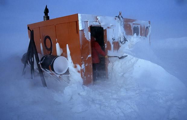 a man is shoveling through the snow in front of an outhouse