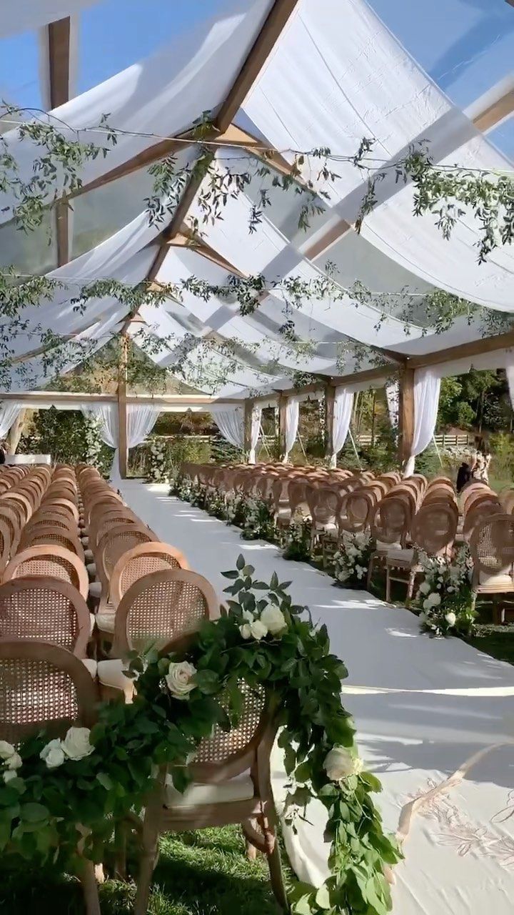 an outdoor wedding venue with white linens and greenery draped over the aisle, chairs are set up on either side of the aisle