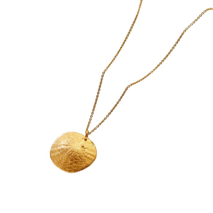 The Gold Plated Large Sand Dollar Necklace is a beautifully crafted piece of jewellery, capturing the delicate and intricate design of a sand dollar in precious metal. The pendant itself i an organic circular disc, textured to resemble the natural patterns found on a real sand dollar, with subtle details that highlight its elegance.   The necklace is made from Sterling Silver plated in a warm 18ct yellow gold, suspended from a fine chain that complements the pendant's minimalist yet sophisticated appearance.  Whether worn alone or layered with other pieces, the Large Sand Dollar Necklace is a versatile and striking addition to your jewellery collection making it a perfect accessory for those who appreciate both nature and refined elegance. 925 Sterling Silver with 18ct yellow gold plating. Elegant Circle Hammered Necklaces, Elegant Hammered Circle Necklace, Nature-inspired Round Etched Jewelry, Hammered Brass Coin Pendant Necklace, Round Metal Medallion Necklace, Tarnish Resistant, Hammered Round Medallion Necklace As Gift, Elegant Hammered Medallion Necklace Gift, Round Metal Medallion Necklace Tarnish Resistant, Elegant Hammered Medallion Necklace