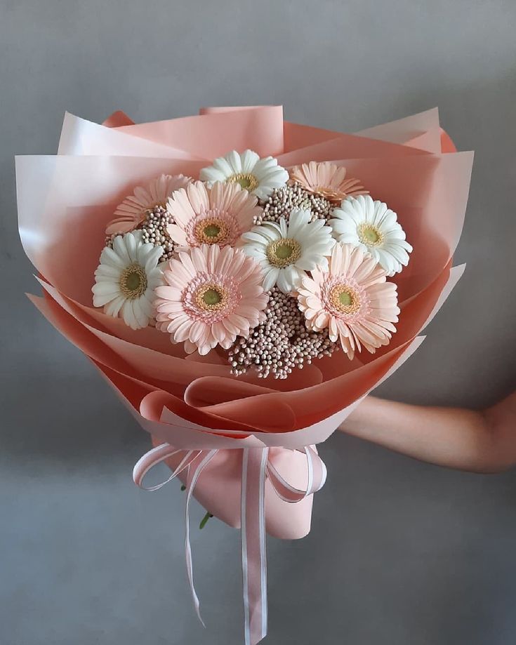 a bouquet of pink and white flowers is held by someone's hand on a gray background