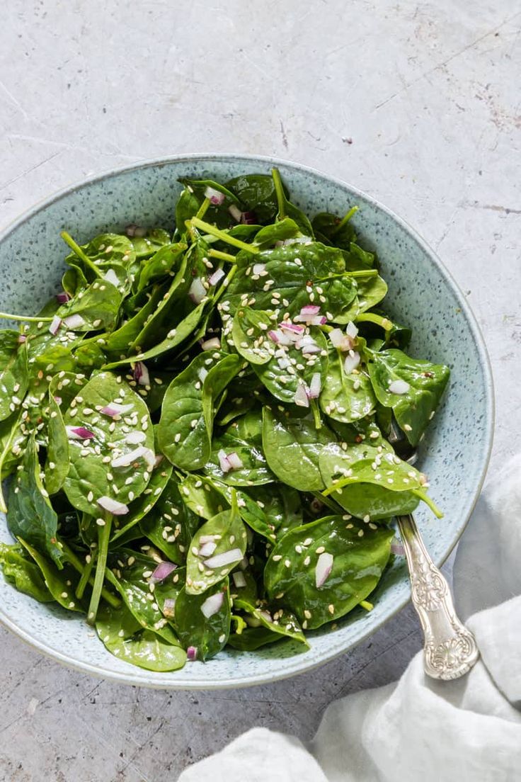 a blue bowl filled with spinach and topped with red onion sprinkles