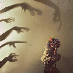 a woman sitting on the ground in front of shadows of hands coming out of her body