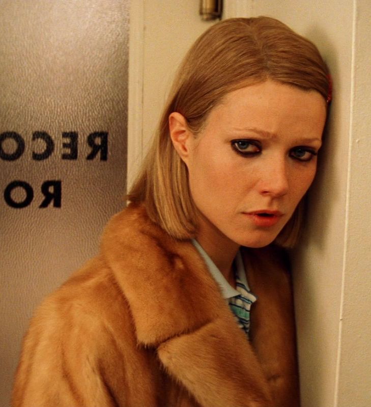 a woman in a fur coat leaning against a wall with her hand on the door