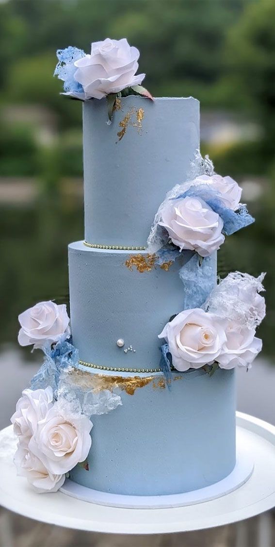 a three tiered blue wedding cake with white flowers