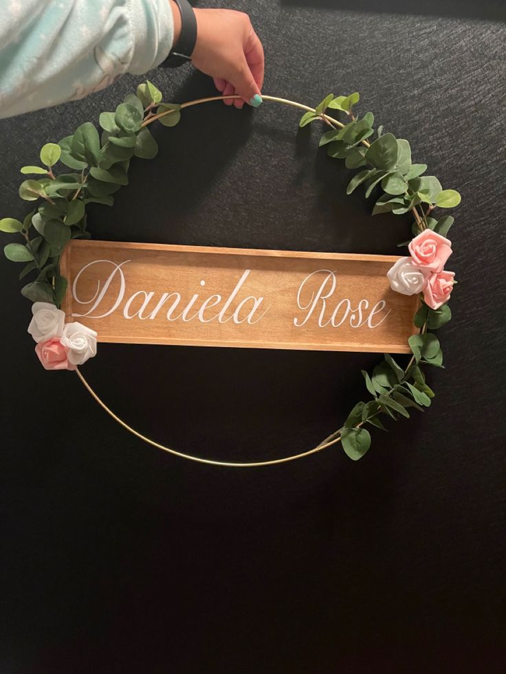 a wooden sign that says danielle rose with flowers on it and greenery around the edges