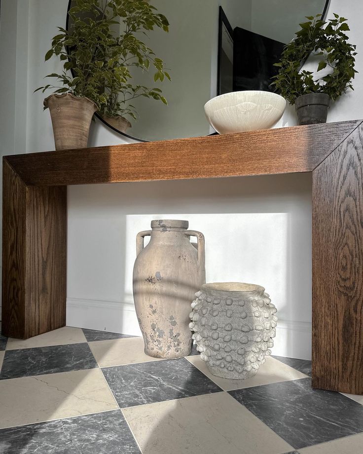 a vase sitting on top of a wooden table next to a mirror and potted plants