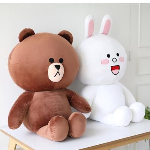 two stuffed animals sitting next to each other on top of a wooden table in front of a white wall