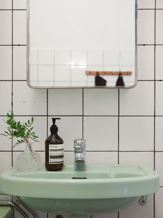 a bathroom sink sitting under a mirror next to a green chair and potted plant