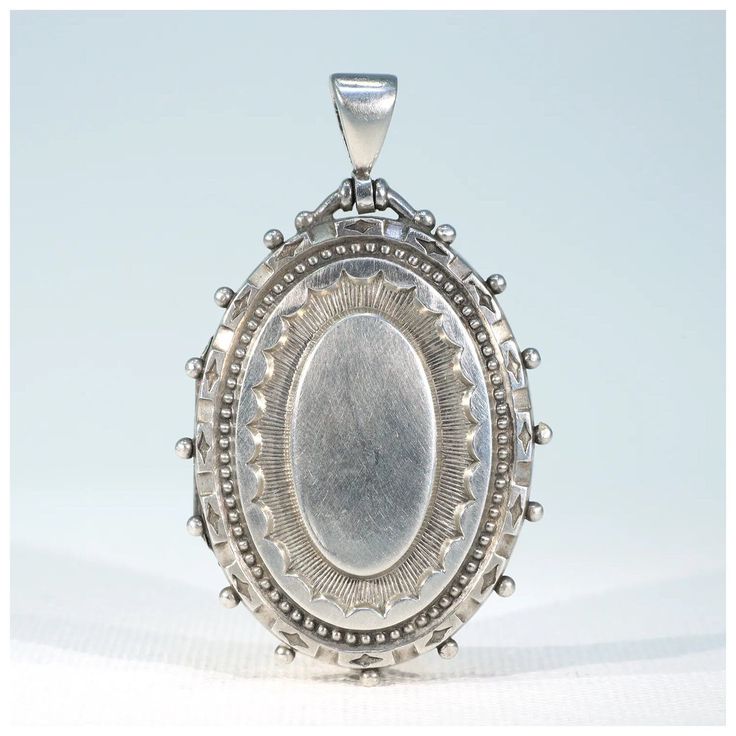 A silver locket, an icon of the Victorian Era. It can be worn on a collar for a dressy look that rivals any diamond dribbles, it can be worn on a chain or even a black ribbon with jeans and a flip flops or over a turtle neck to great effect. It's an essential that's far from basic. This wonderful locket was hand crafted in about 1880, it has panache, style that is. It was most likely made in the English jewelry center of Birmingham, but it has no marks, we've carefully tested it to verify that it is, indeed, sterling silver. The locket has a wonderful sunburst with geometric details repoussed in the front and a soft and smooth rounded oval back. This locket opens to reveal two frames ready to hold your personal photos. The locket measures 55 mm north to south including the bale and 33.8 mm Luxury Memorial Locket Jewelry, Silver Locket Necklace For Formal Occasions, White Gold Medallion Jewelry With 17 Jewels, Elegant Hallmarked Pendant Locket Necklace, Victorian White Gold Pendant Jewelry, Victorian Style White Gold Pendant Jewelry, Elegant Hallmarked Locket Necklace For Formal Occasions, Classic Locket Jewelry For Wedding, Vintage White Gold Oval Pendant Jewelry