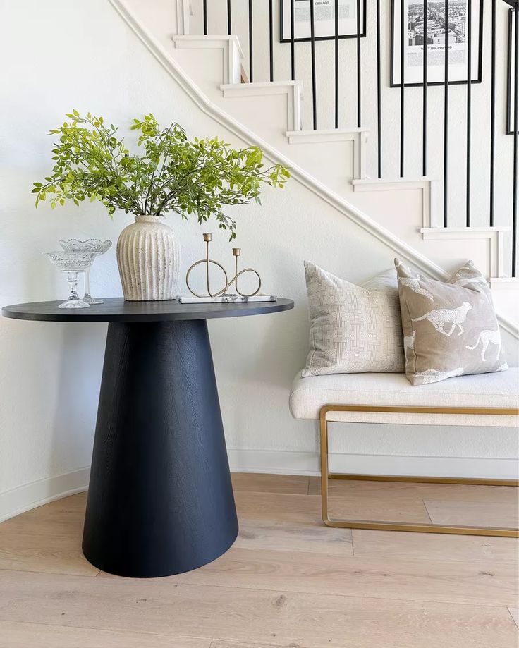 a black table with two vases on it next to a stair case and chair