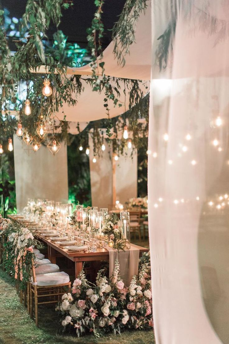 a long table set up with flowers and candles for an outdoor wedding reception at night