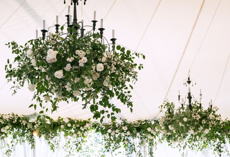 flowers hanging from chandelier in tent with white walls and windows behind the ceiling