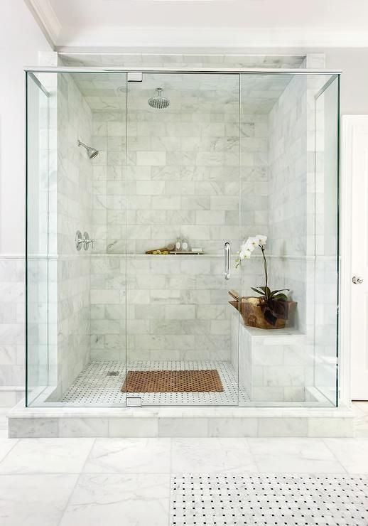 a walk in shower sitting next to a white tiled wall and floor with a potted plant on the side