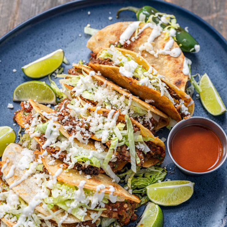 three tacos on a blue plate with limes and sauce