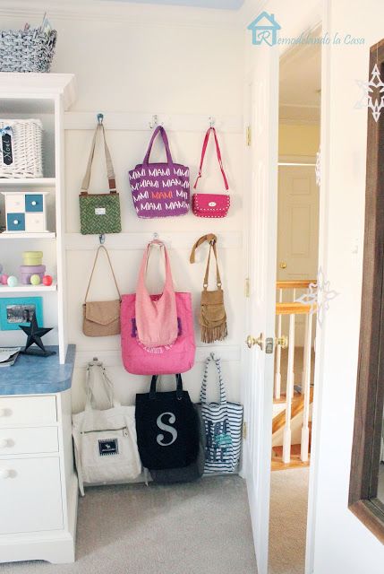 several purses and bags hanging on the wall in a room with white cabinets, drawers and shelves