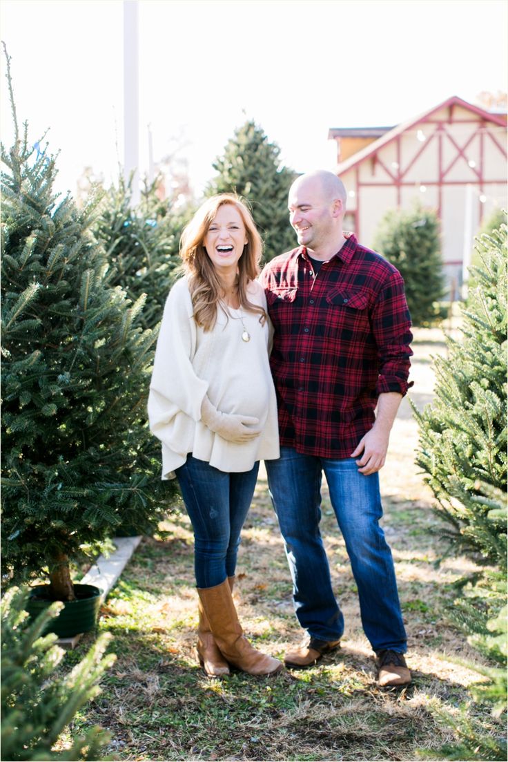 a pregnant couple standing next to each other in the middle of a christmas tree farm