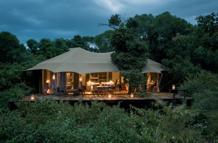 a tented area with tables and chairs in the middle of trees at night time