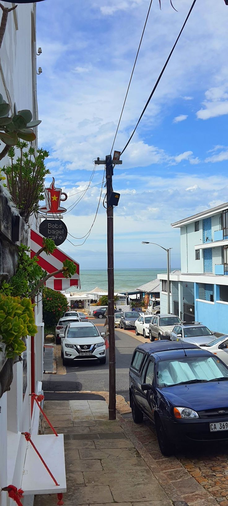 cars parked on the side of a street next to a blue building and ocean in the background