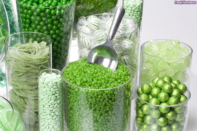 green candies and candy are arranged in glass vases on the table with silver spoon