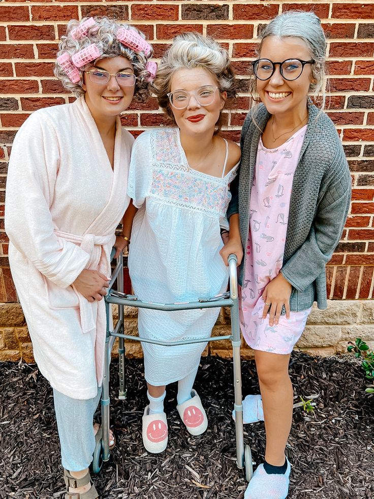 three women standing next to each other in front of a brick wall with a walker