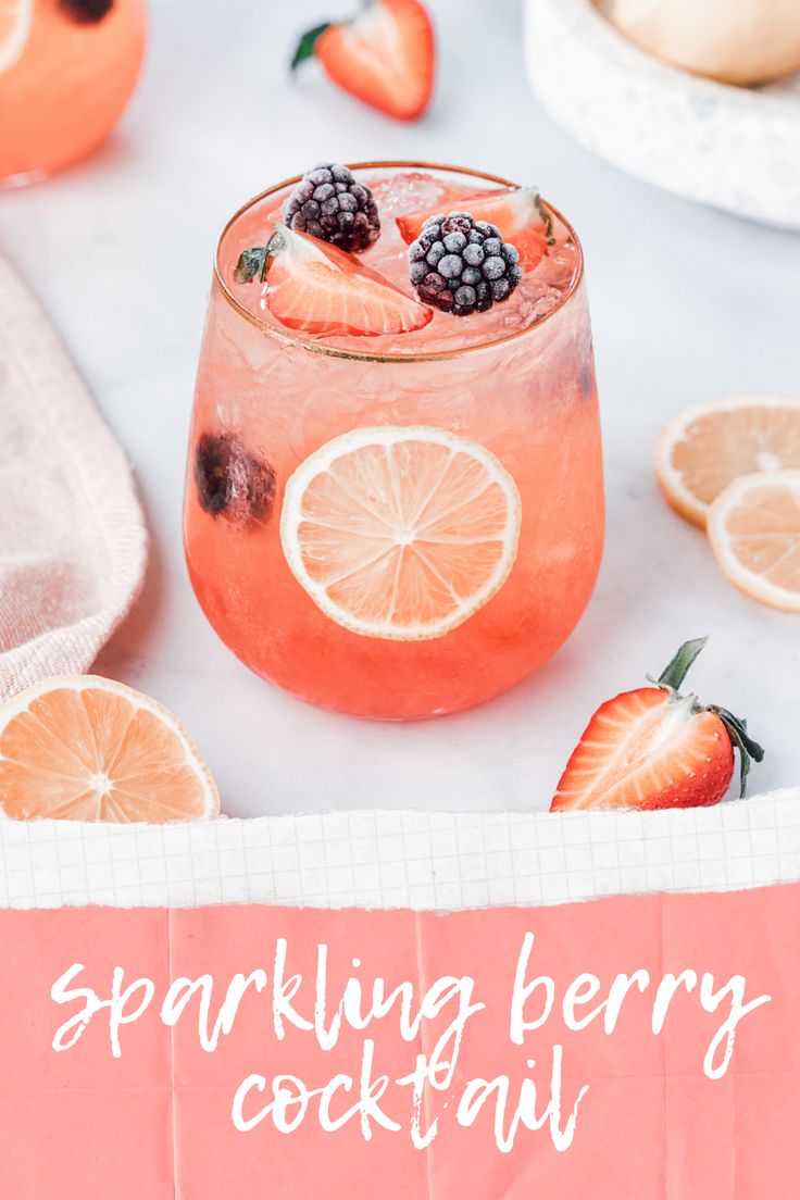 a pink cocktail with berries and lemons on the rim next to sliced oranges