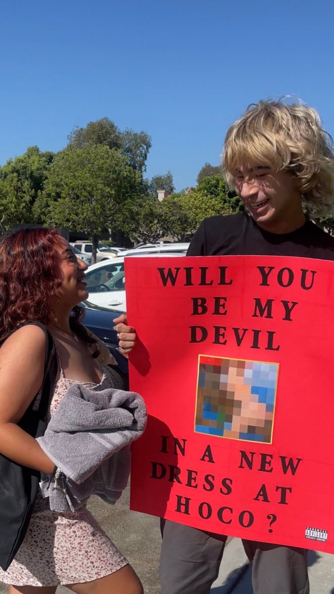 two people holding a sign that says will you be my devil in a new dress at hoco?