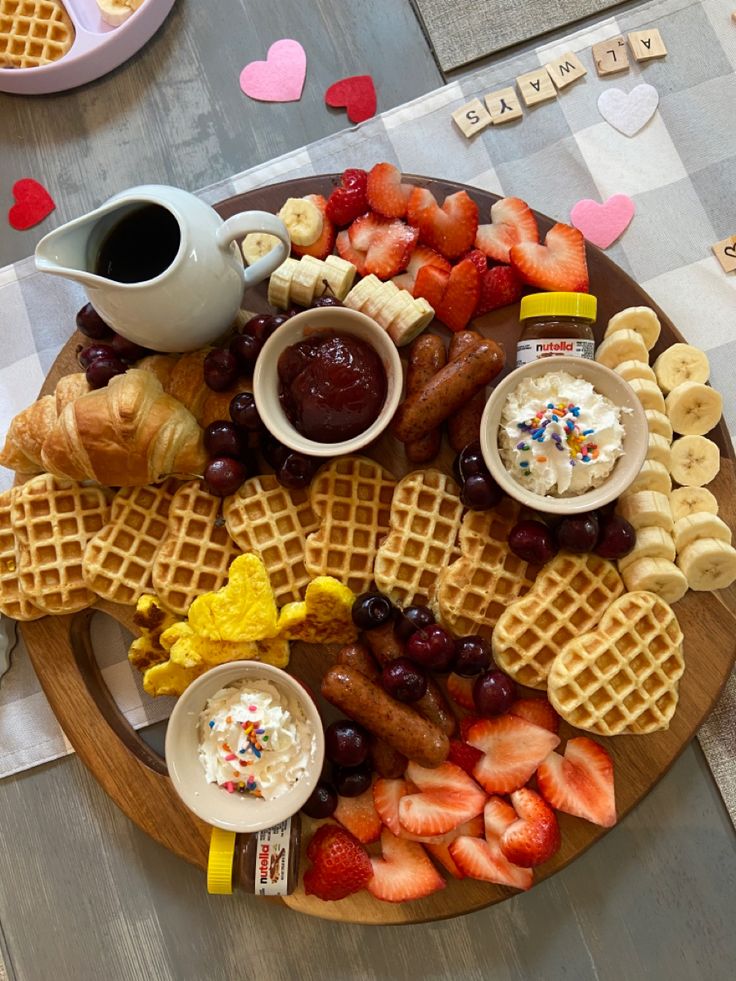 a wooden plate topped with waffles, fruit and other foods on top of a checkered table cloth