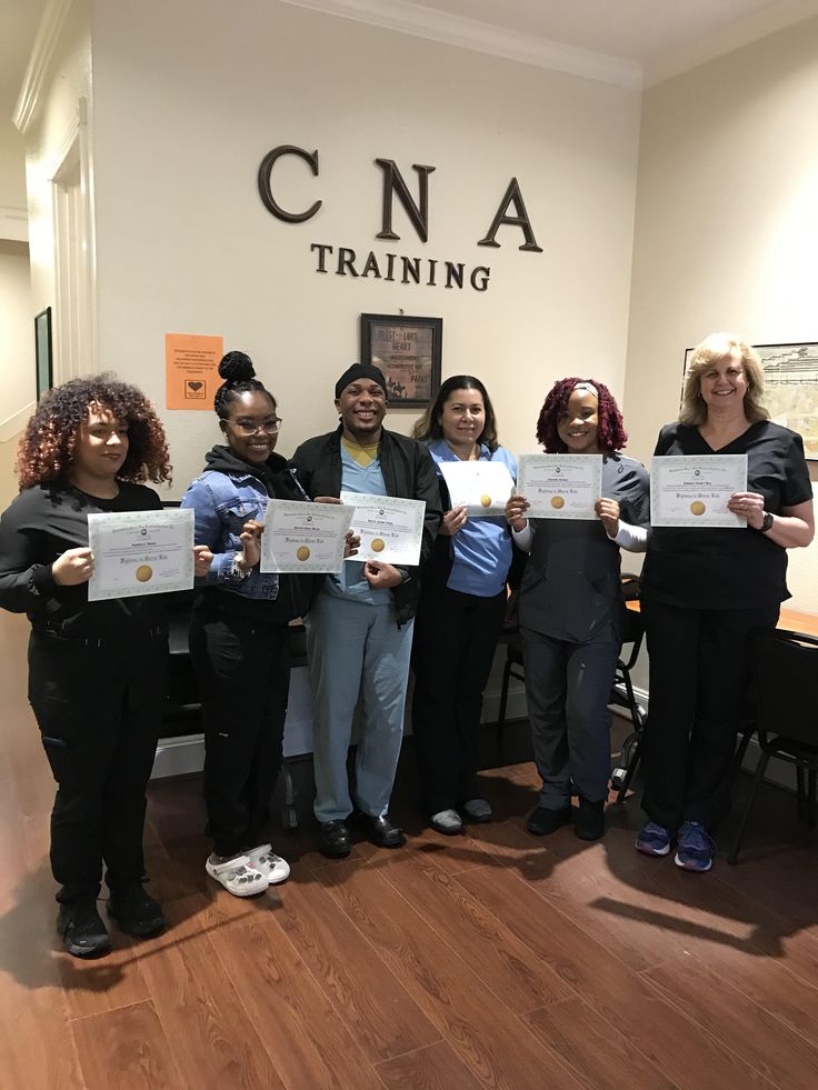 five people holding up their diplomas in front of a wall with the words cna training on it