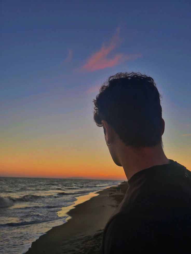 a man standing on top of a sandy beach next to the ocean at sun set