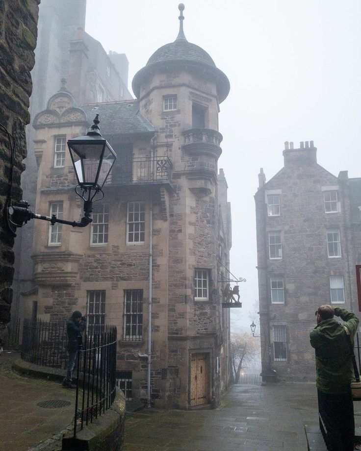 an old stone building on a foggy day with two people standing in the doorway