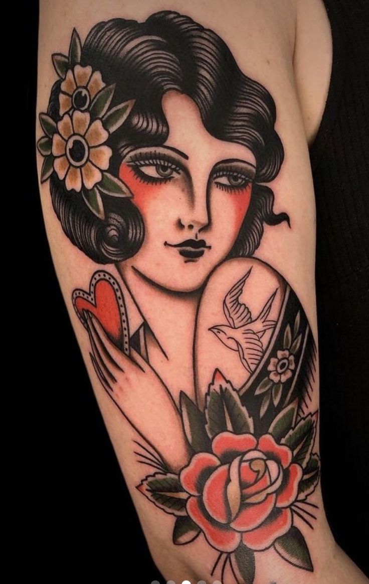 a woman's arm with tattoos on it and flowers in her hair, holding a heart