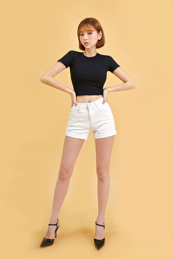 a woman in black shirt and white shorts standing with her hands on the hips while wearing high heeled shoes