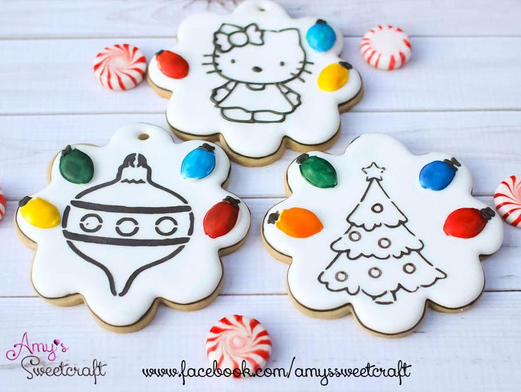 three decorated christmas cookies sitting on top of a white wooden table next to candy canes