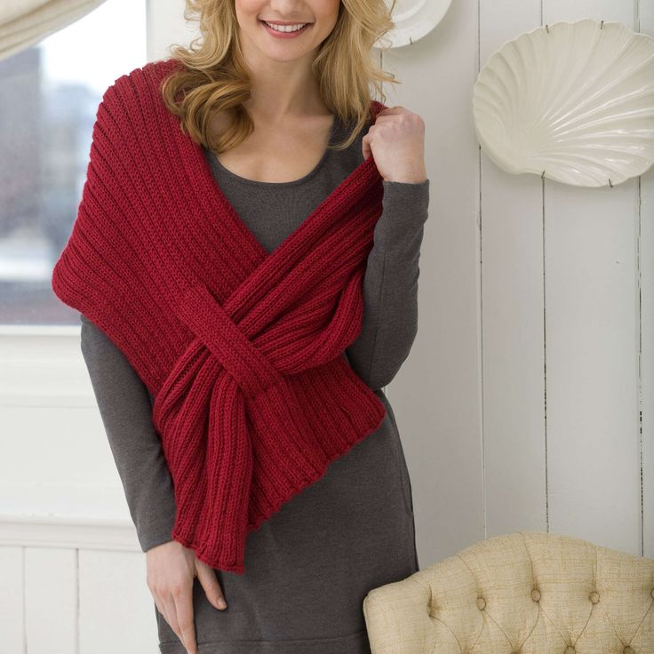 a woman standing next to a chair wearing a red knitted wrap around her neck