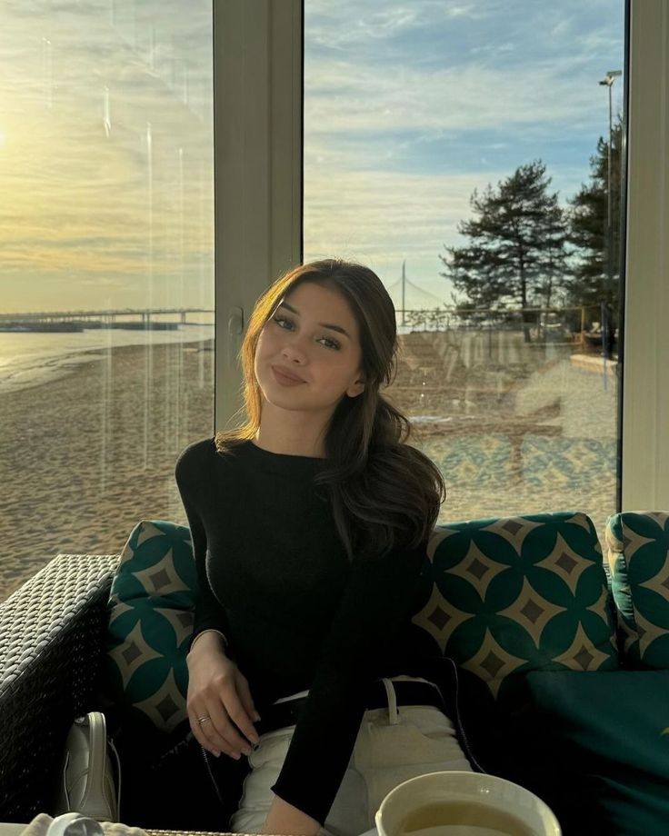 a woman sitting at a table with a cup of coffee in front of a window