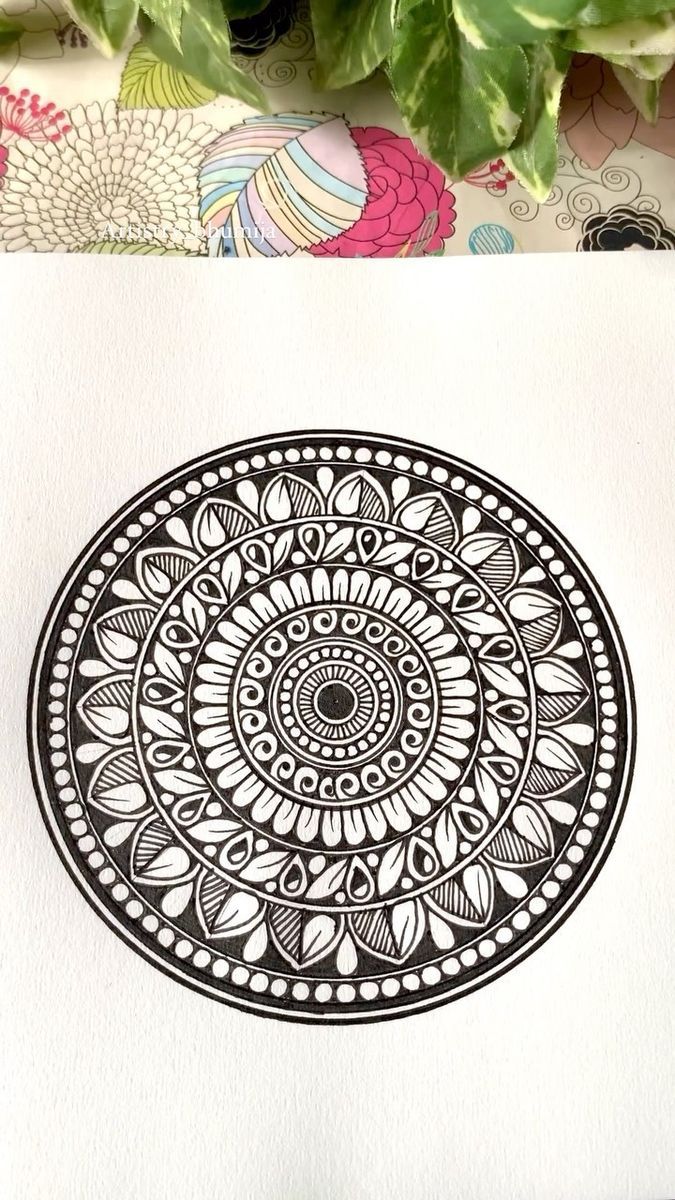 a black and white drawing of a circular design on paper next to a potted plant