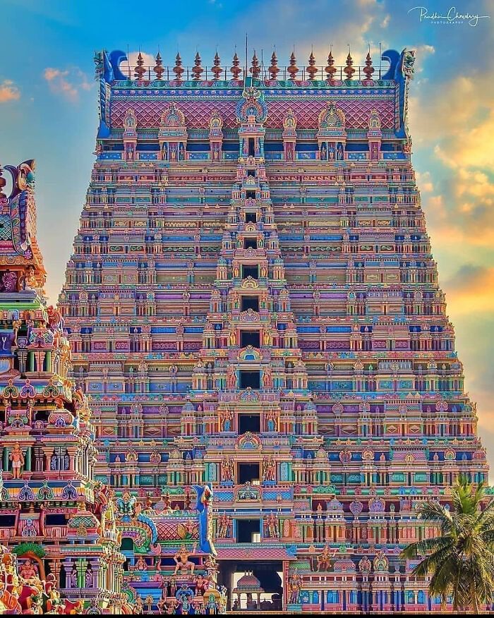 an ornately decorated hindu temple with palm trees in the foreground and clouds in the background