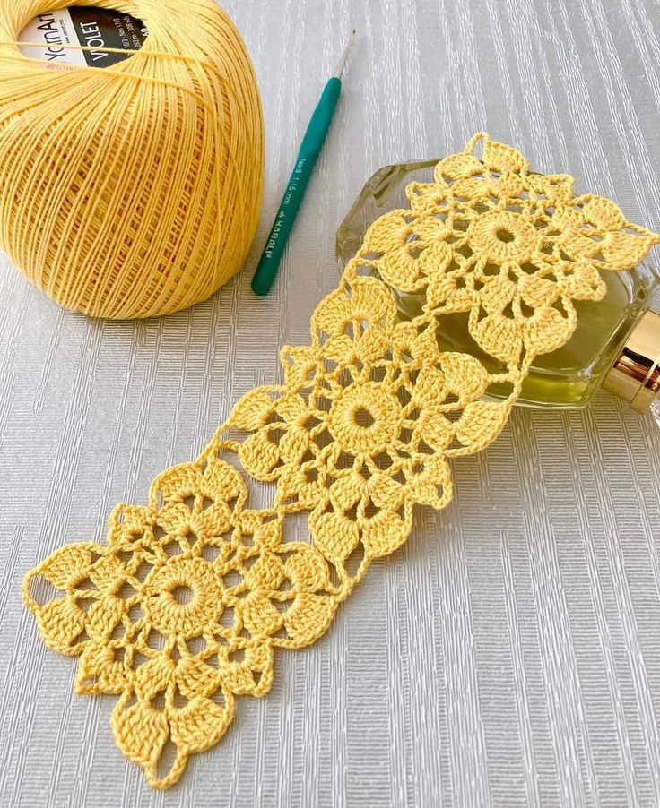 a yellow crochet doily next to a ball of yarn and a bottle of perfume