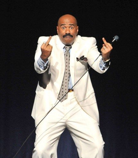 a man in a white suit and tie giving the peace sign while standing on stage