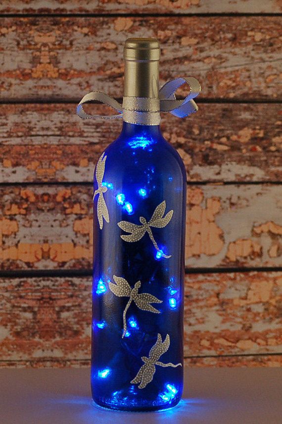 a blue glass bottle with lights in the shape of dragonflies on it, sitting on a table