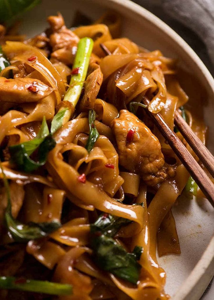 a white bowl filled with noodles and meat next to chopsticks on a table