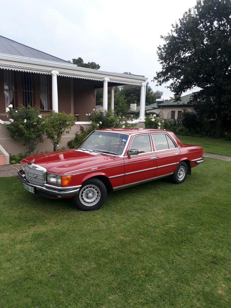 a red car is parked in front of a house on the grass near some bushes